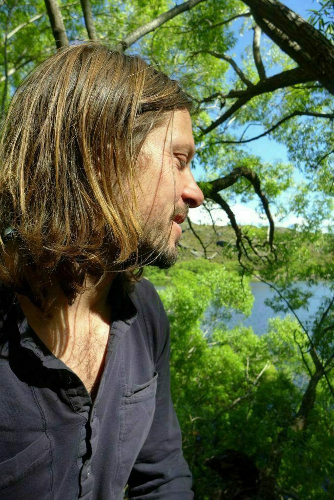 Vincent in the lush nature looking back towards a big tree and lake.