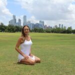 Olivia in a white dress sitting on the grass in a park.