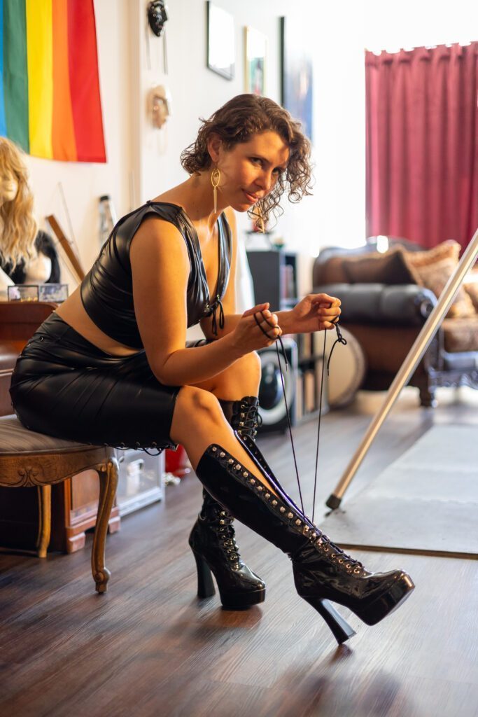 Goddex Electra wearing black leather and tying the laces of her high heel boots.