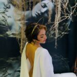 Angela in a white robe kneeling on a white sofa.