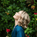 Venus Rose ina blue dressing looking up and holding a rose