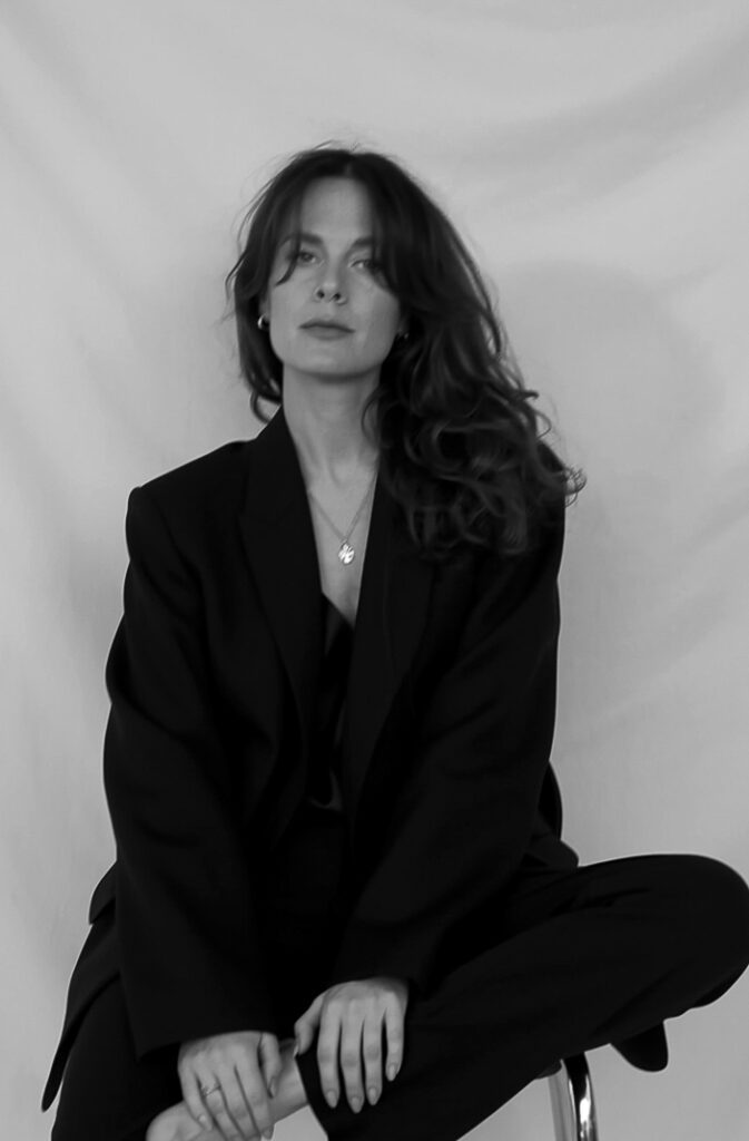 Black/white shot of calypso in dark formal clothing. Sitting on a chair looking professional and serious.