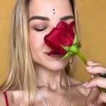 Close-up of her face, smelling a red rose.