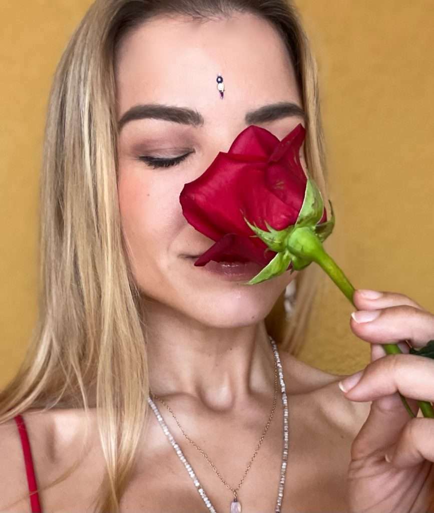 Close-up of her face, smelling a red rose.