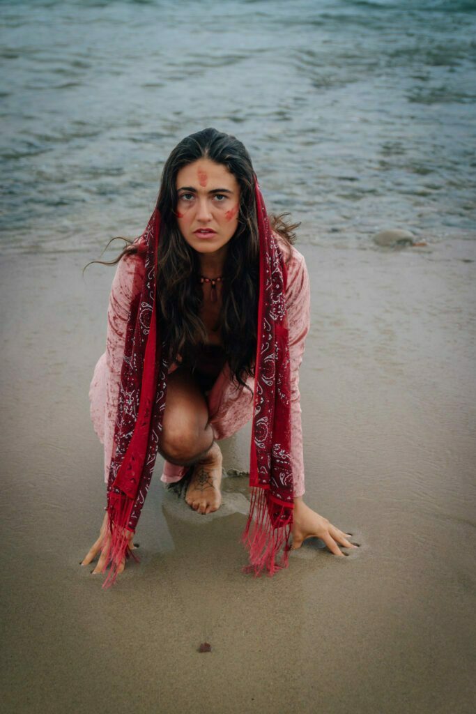 Anna Ruth squatting on the beach in water with red paint on her face.