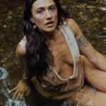 Anna in a white wet shirt sitting in a river.