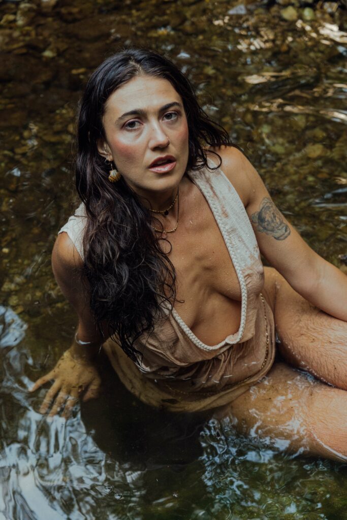 Anna in a white wet shirt sitting in a river.