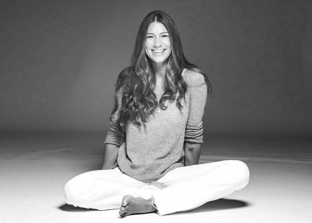 Amy with a big warm smile sitting cross-legged.