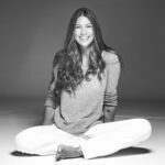 Amy with a big warm smile sitting cross-legged.