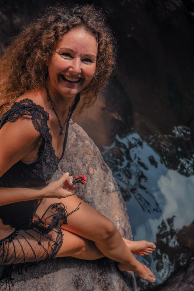 Sitting on a rock with a big smile holding a red flower in her hands.