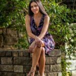 Stephanie in an elegant purple dress sitting on a rock wall.