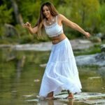 Walking in a river, balancing on rocks, wearing a white top and white long skirt.