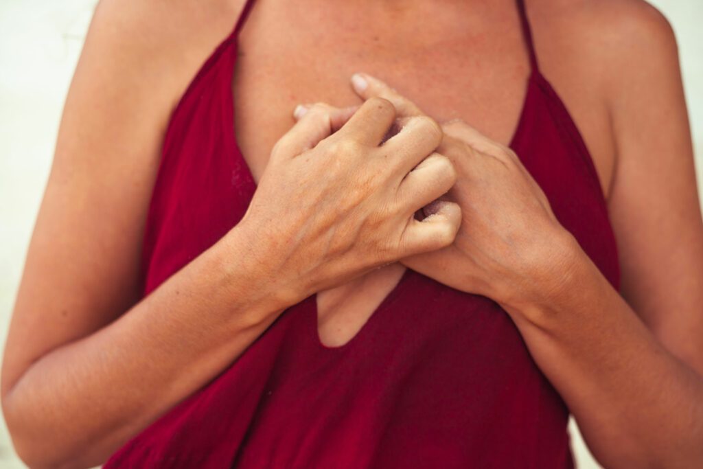 Close up of a chest in red shirt. Her hands are crossed in front of the chest.
