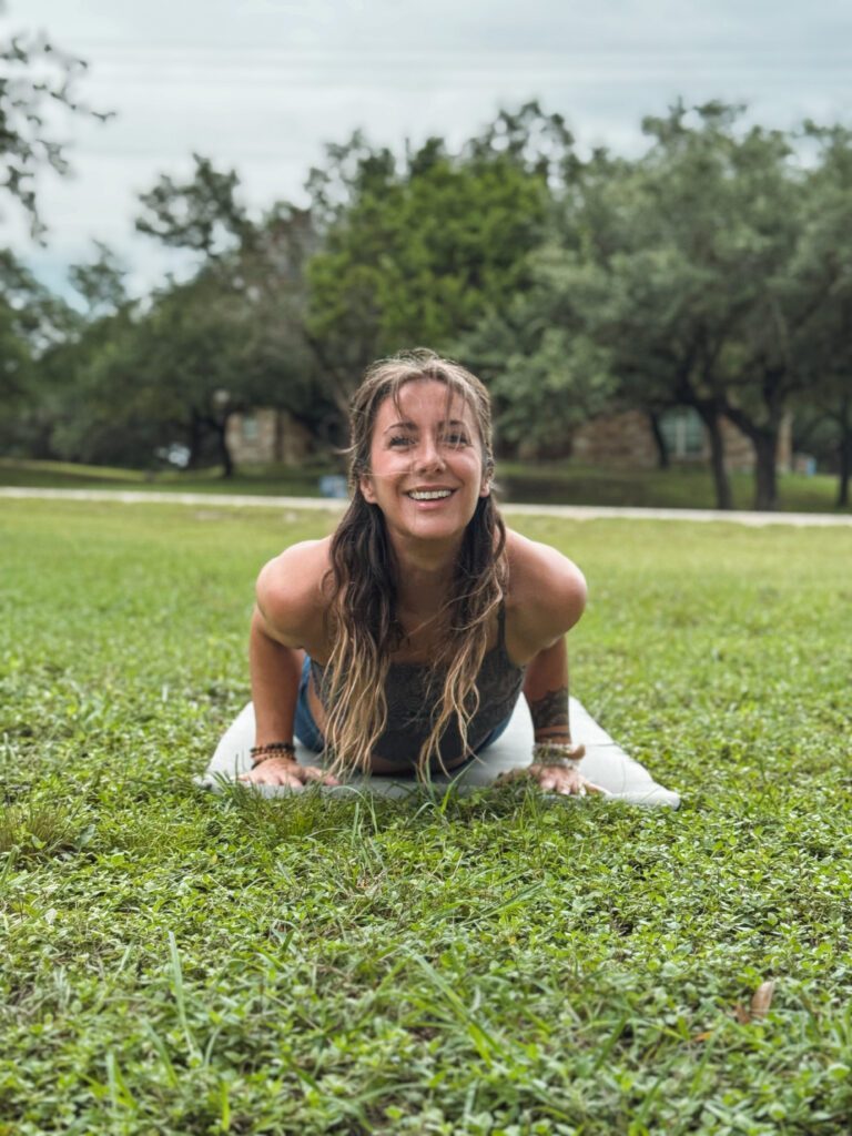Natalie doing an upward dog like yoga pose on the grass.