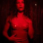 Vixen in a dark room with red light shining on her body.