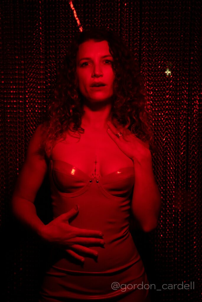 Vixen in a dark room with red light shining on her body.