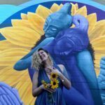 Yello-blue painted wall with Seriph in the front holding sunflowers.