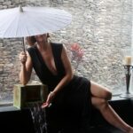 Sitting on a ledge holding an umbrella above her head.