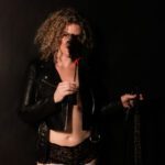 Maya Rose wearing black panties and a black jacket while holding a black feather in front of her face.