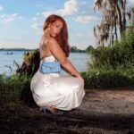 Opal Wolfe by a lake squatiing in a white beautiful dress.