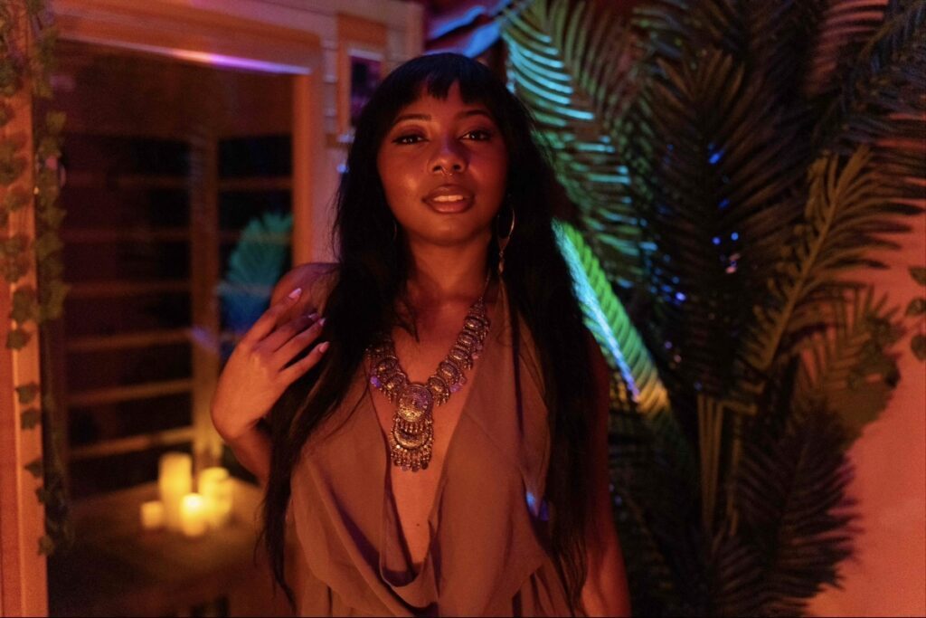 Seraphina in a room with exotic lighting and a big houseplant.