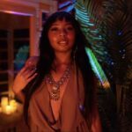 Seraphina in a room with exotic lighting and a big houseplant.