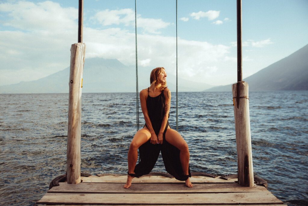Artistic shot of Joy Shakti sitting on a swing at the end of a basic wooden pier.