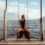 Artistic shot of Joy Shakti sitting on a swing at the end of a basic wooden pier.