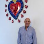 Phil in jeans standing in front of a wall with an artpiece.