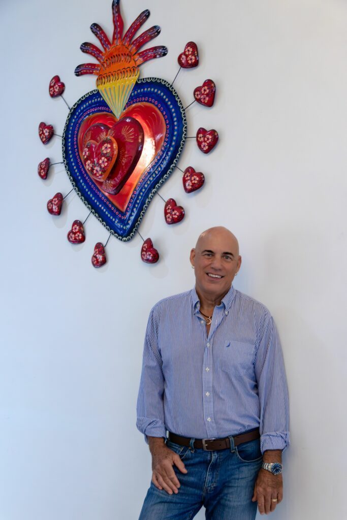 Phil in jeans standing in front of a wall with an artpiece.