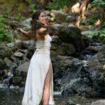 Dr Rose standing in a river wearing a long white dress.