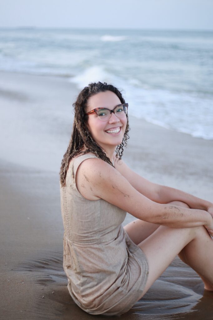Liz sitting in the sand by the sea.