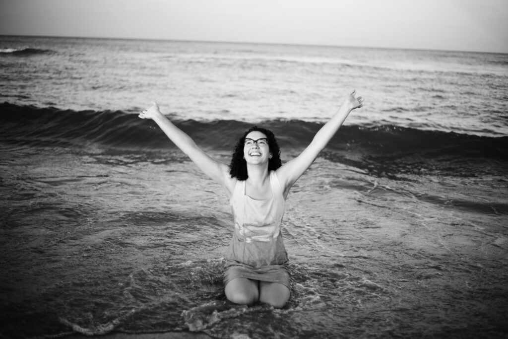 Kneeling in the sea with arms lifted towards the sky.