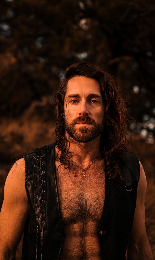 Sam in a leather vest looking strong and serious.