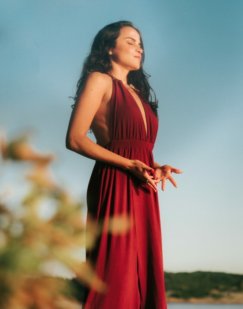 Amara in a long red dress taking a deeo breath in.