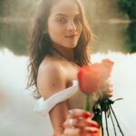 Holding red roses by the lake.