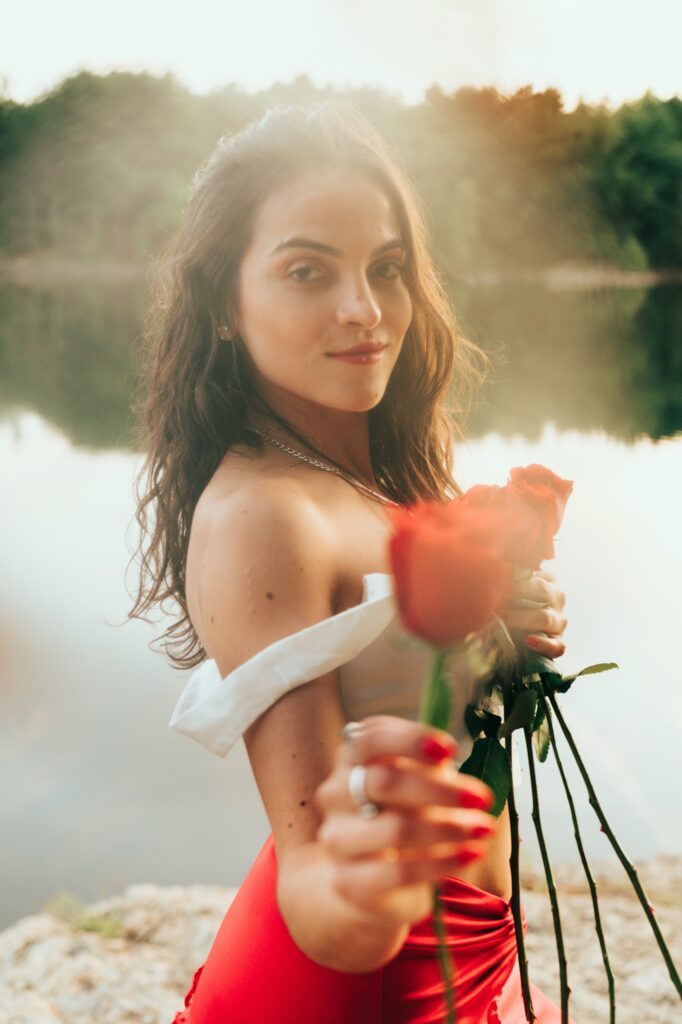 Holding red roses by the lake.