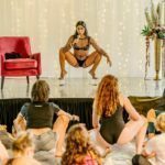 Selene on the stage, squatting in front of a group of women.