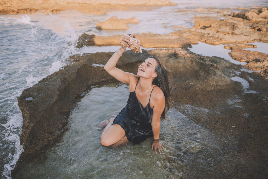 Keren in a natural pool pouring water on herself from a seashell.