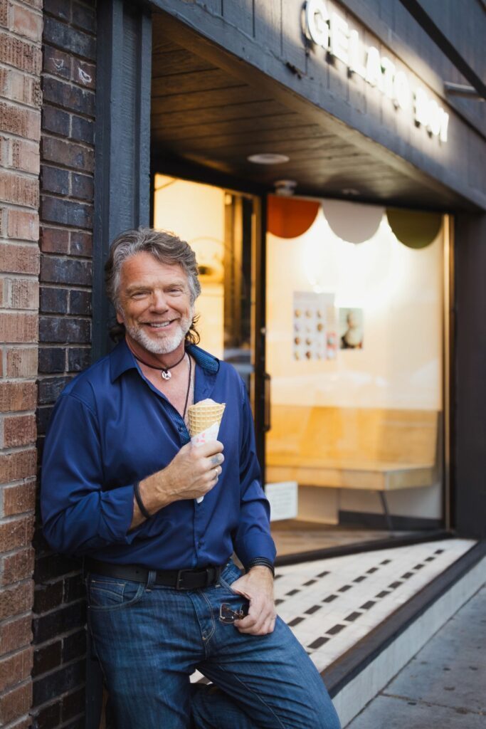 Leaning against a wall of an ice-cream shop while eating one.