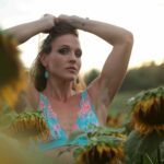 Tantra & Intimacy Coach standing in a field of sunflowers in a blue swimsuit-like top.