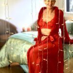 Luminara sitting on the edge of the bed in a red robe and lingerie.