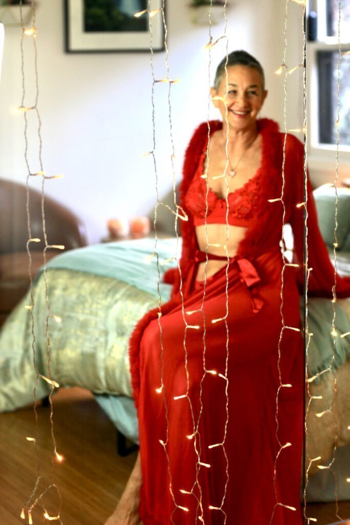 Luminara sitting on the edge of the bed in a red robe and lingerie.