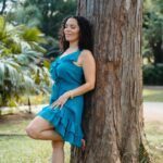 Triambika in a blue dress leaning against a big tree.