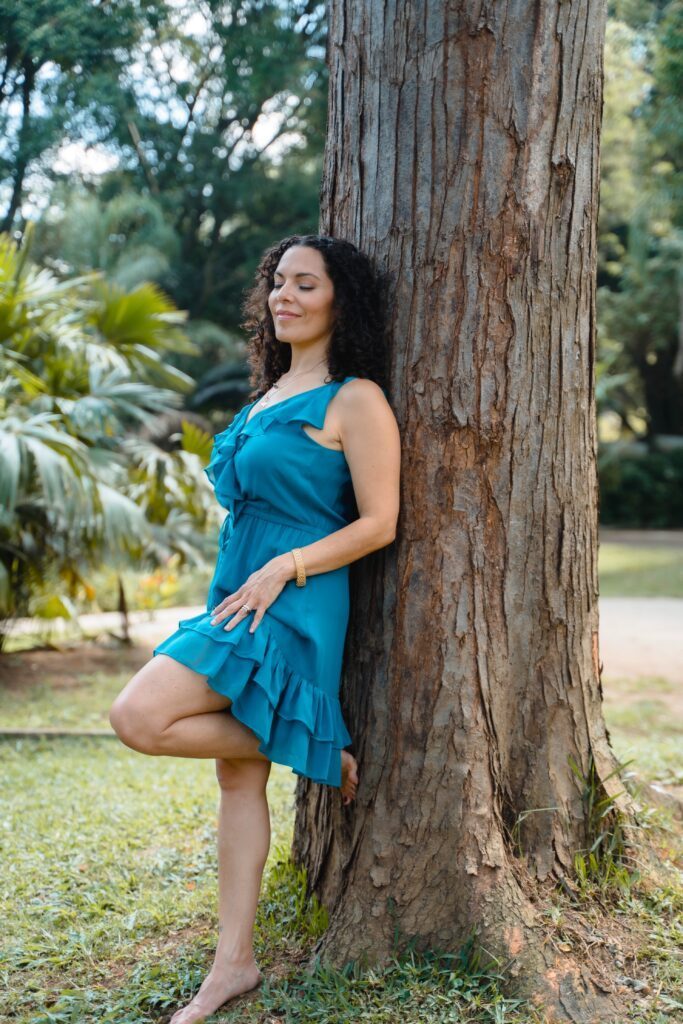 Triambika in a blue dress leaning against a big tree.