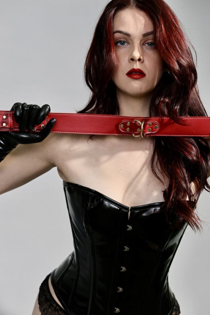 Satine Laurent in full leather holding a red belt.