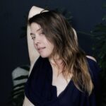 Juliette Bloom in a black top with her arm over head.