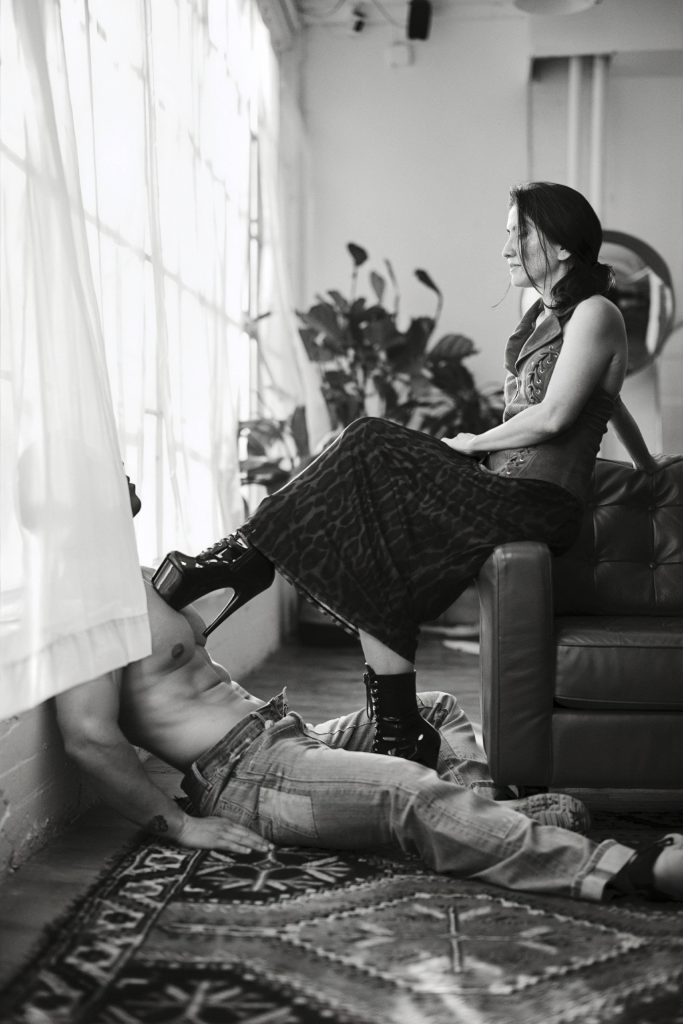 Male client on the floor. Kalika has her foot in a platform shoe on top of his chest.