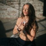 Michella in sunlight with her hands crossed in front of her naked chest.