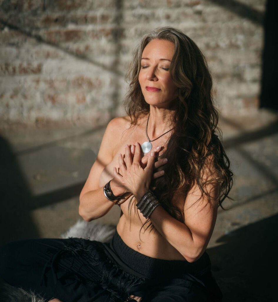 Michella in sunlight with her hands crossed in front of her naked chest.